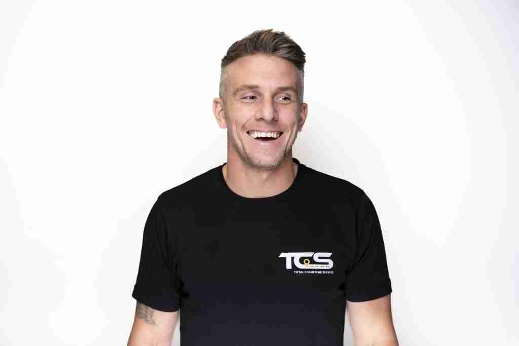 Commercial Photographer Peterborough | Nate Lansdell 117 A man with short hair smiles while wearing a black t-shirt with a logo, against a plain white background.